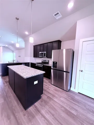 a kitchen with stainless steel appliances granite countertop a refrigerator a sink a stove and a wooden floor