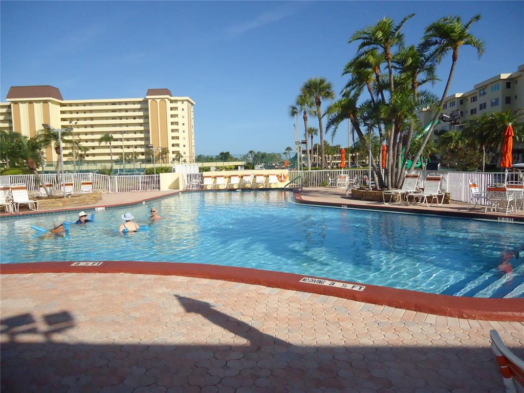 4550 Cove Circle, Unit 405 Madeira Beach, FL 33708 - Photo 10 of 20 a view of a swimming pool with a lawn chairs under palm trees