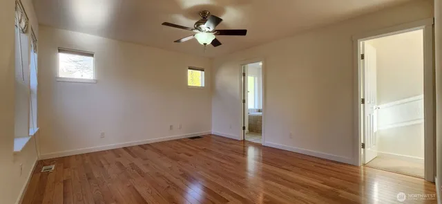 an empty room with wooden floor chandelier fan and windows