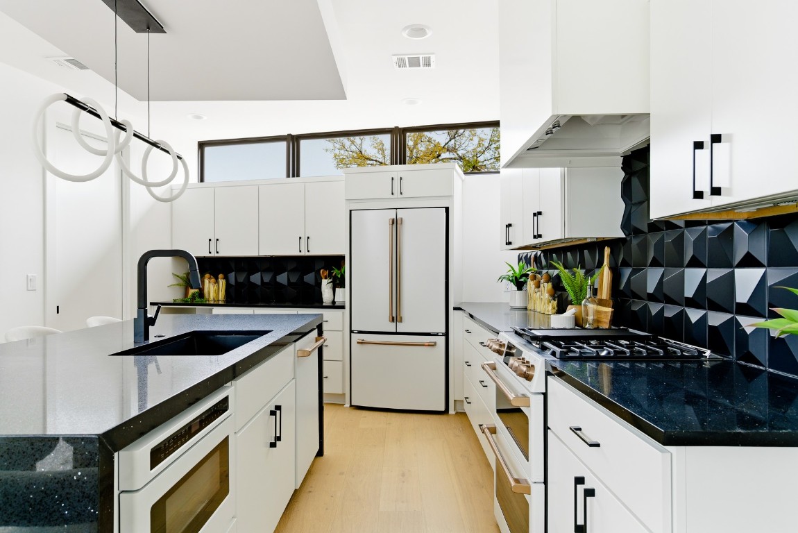 4613 Bolm Road Austin, TX 78702 - Photo 16 of 40 Kitchen with dark stone countertops, a center island with sink, premium appliances, hanging light fixtures, and white cabinetry