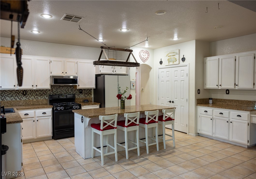 212 Malcolm Street Henderson, NV 89074 - Photo 10 of 47 Large Open Kitchen with white cabinets, black gas stove, light tile patterned flooring, a kitchen breakfast bar, and a textured ceiling