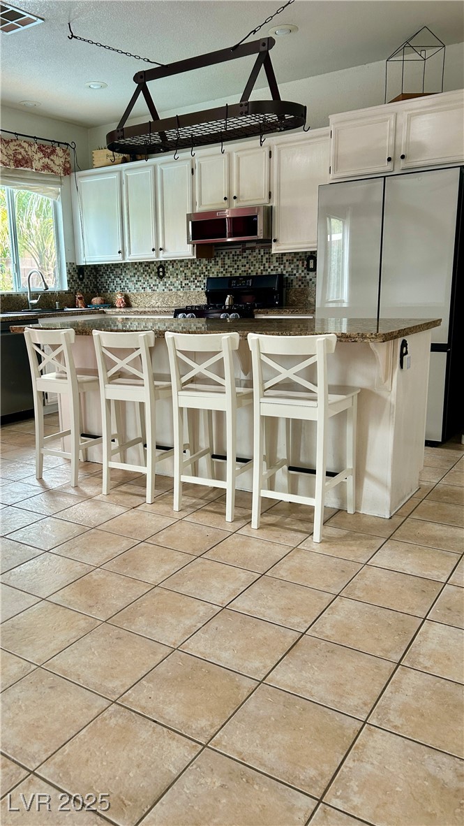 212 Malcolm Street Henderson, NV 89074 - Photo 37 of 47 Kitchen with a kitchen bar, white cabinetry, black appliances, light tile patterned flooring, and tasteful backsplash