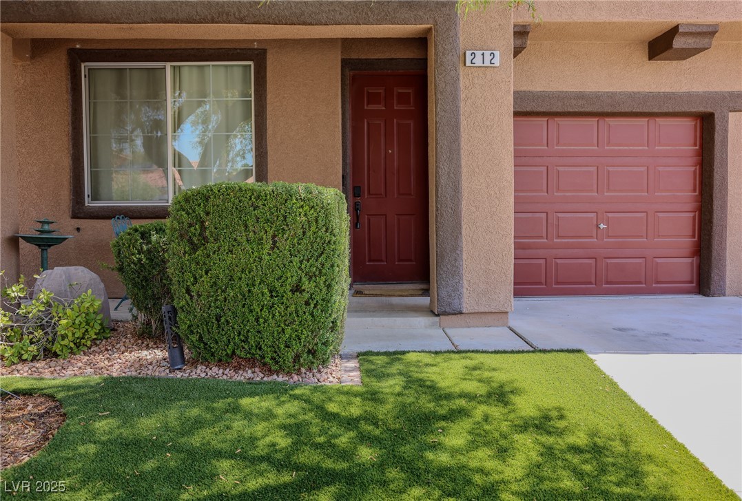 212 Malcolm Street Henderson, NV 89074 - Photo 7 of 47 Doorway to property with stucco siding, a garage, driveway, and a lawn