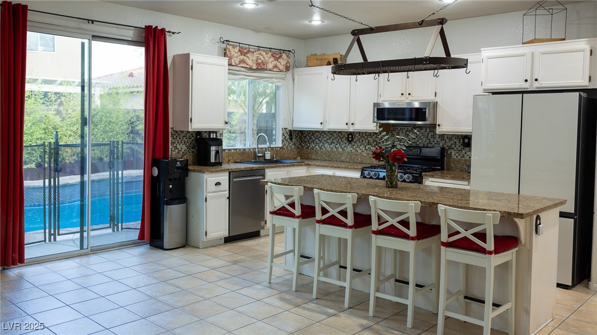 212 Malcolm Street Henderson, NV 89074 - Photo 9 of 47 Kitchen featuring stainless steel appliances, backsplash, a kitchen bar, light tile patterned floors, and white cabinetry
