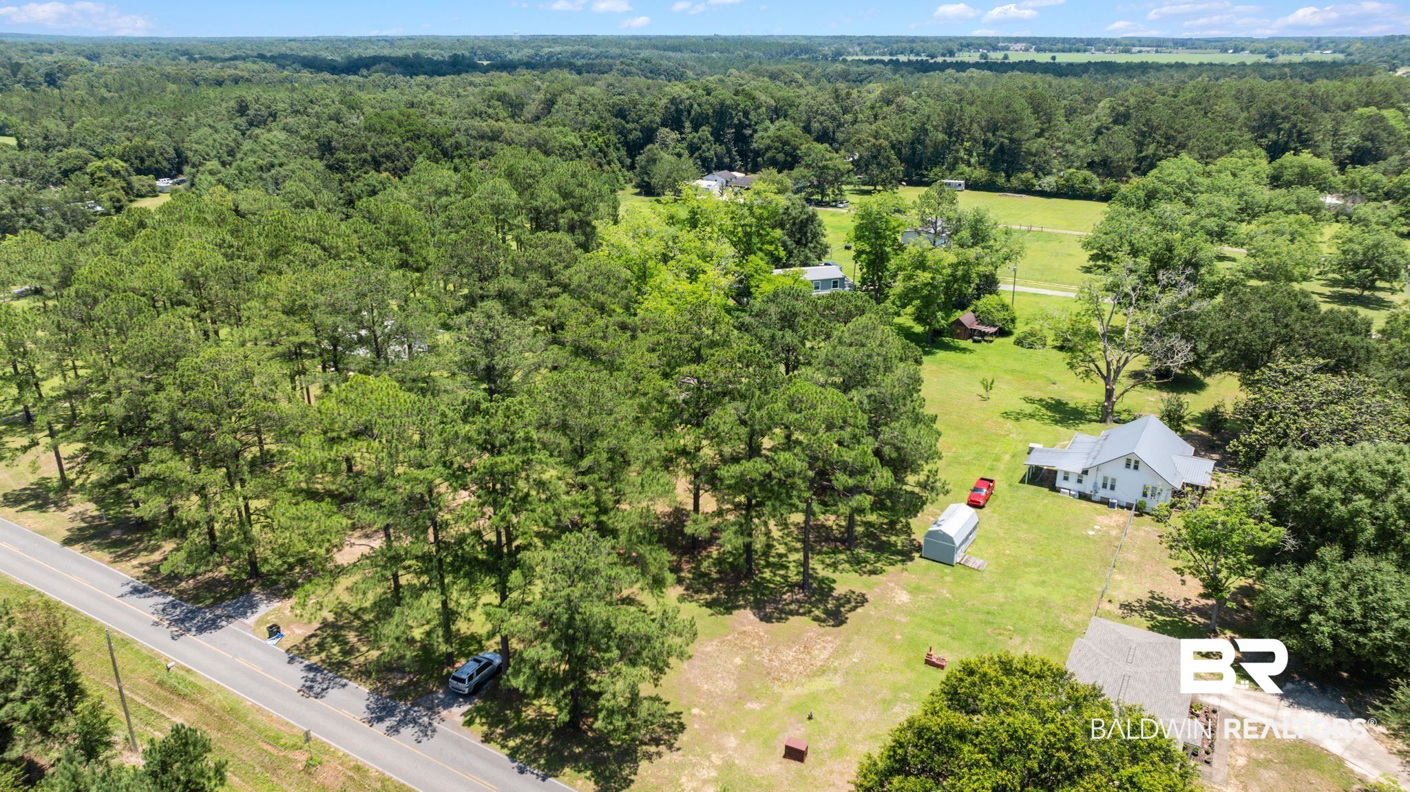 20540 Lacey Road Silverhill, AL 36576 - Photo 32 of 40 Expansive wooded property featuring a white residence with a gabled roof, an unpaved driveway, and a metal storage shed