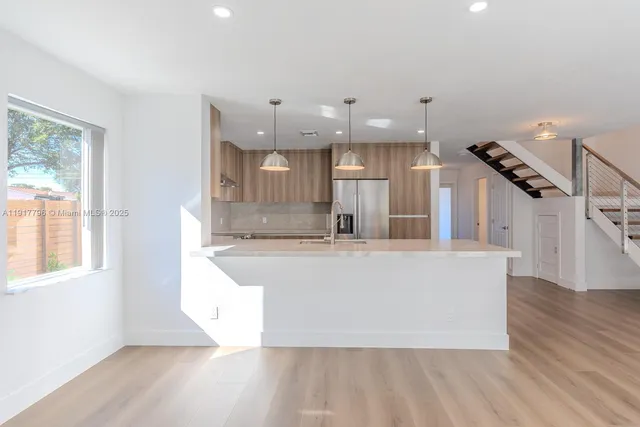 a large white kitchen with wooden floor and a window