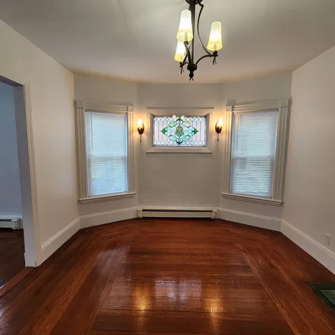 an empty room with wooden floor chandelier fan and windows