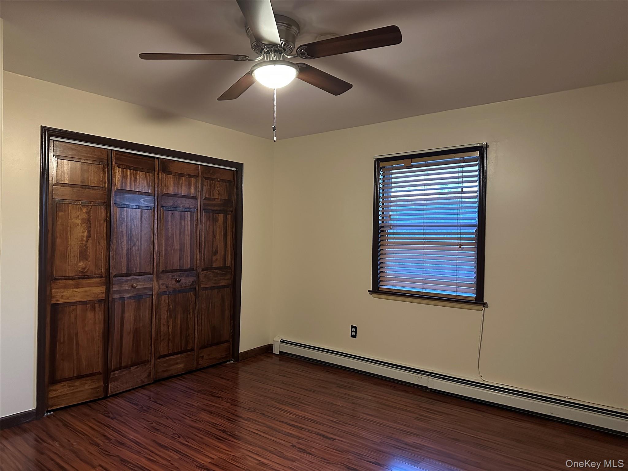62 New Road Newburgh, NY 12550 - Photo 14 of 14 Unfurnished bedroom with a baseboard radiator, a ceiling fan, dark wood-type flooring, and a closet