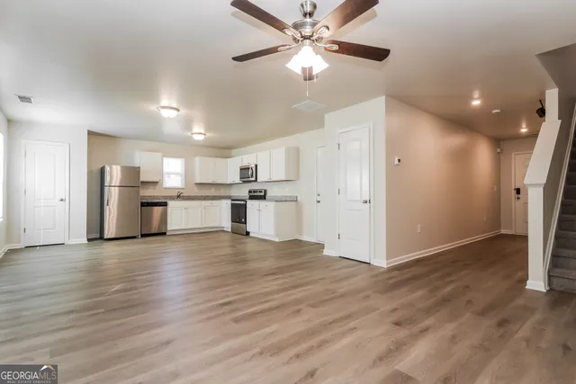 a view of a kitchen with a refrigerator a ceiling fan wooden floor and a kitchen