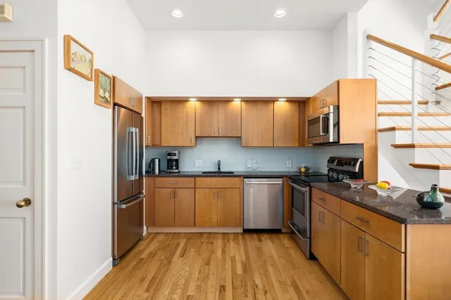 a kitchen with stainless steel appliances granite countertop a refrigerator a sink dishwasher a stove with wooden cabinets and floor