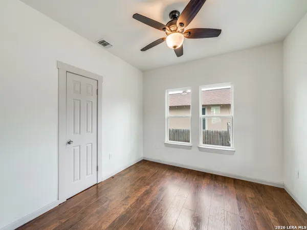 an empty room with wooden floor chandelier fan and windows