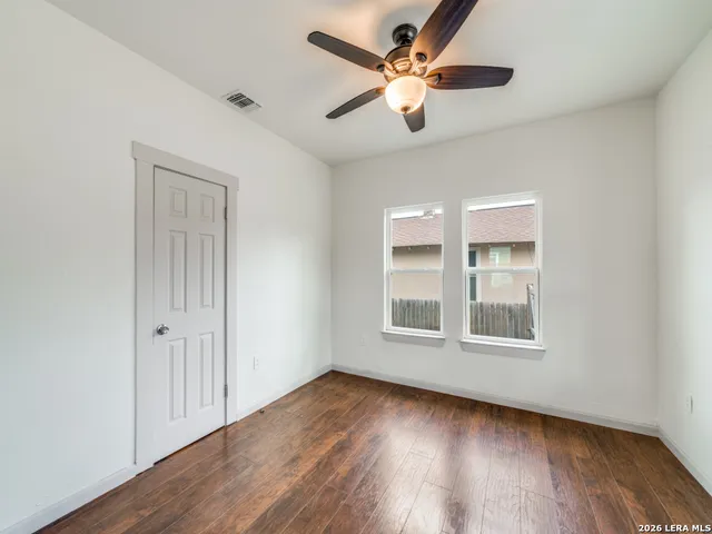 an empty room with wooden floor chandelier fan and windows