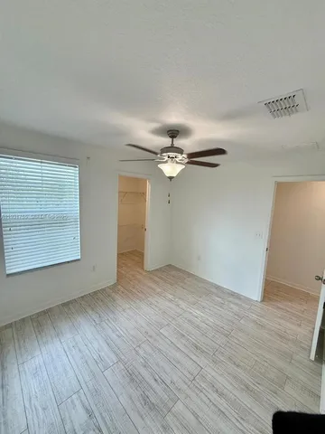 an empty room with wooden floor fan and windows
