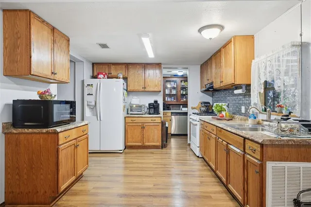 a kitchen with stainless steel appliances granite countertop a refrigerator a sink dishwasher a stove with wooden cabinets and wooden floor