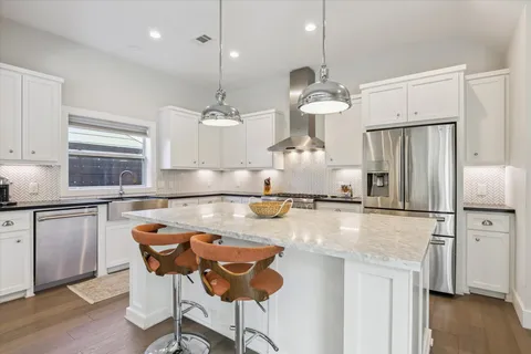 a kitchen with stainless steel appliances granite countertop a sink a stove a refrigerator and island with wooden floor