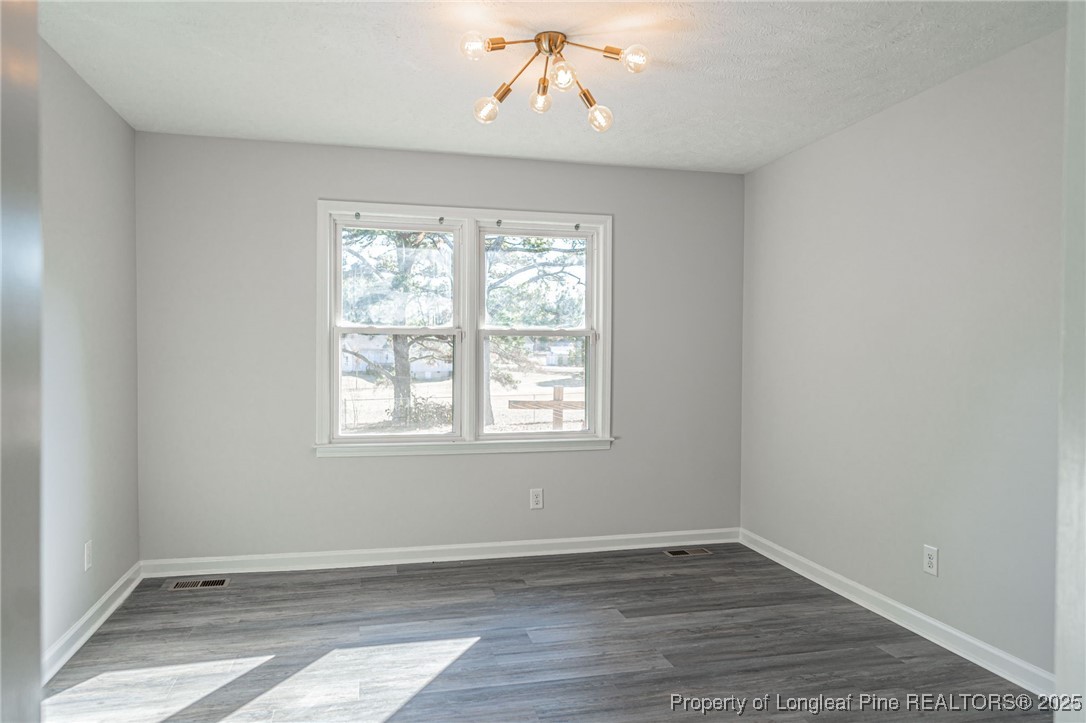 255 Foxcroft Road Whispering Pines, NC 28327 - Photo 13 of 31 an empty room with wooden floor chandelier and windows