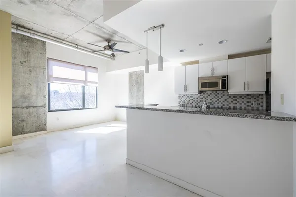 a large white kitchen with kitchen island granite countertop a stove a sink and a granite counter tops with white cabinets next to a window