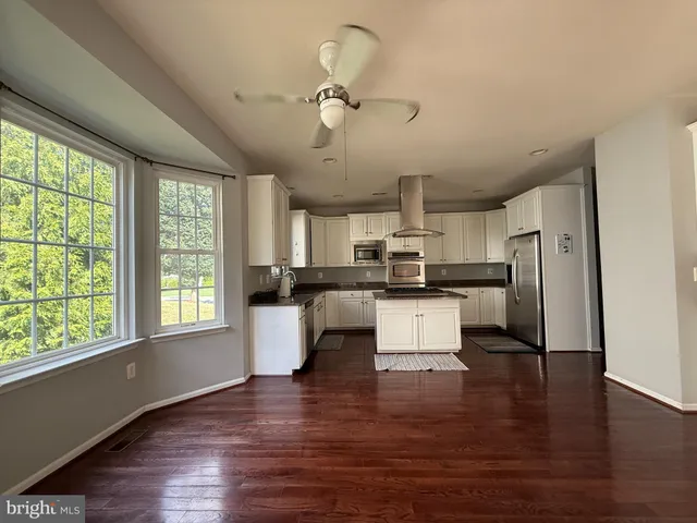 a kitchen with stainless steel appliances kitchen island granite countertop a refrigerator a stove a sink and white cabinets with wooden floor