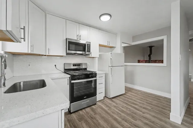 a kitchen with granite countertop a refrigerator stove and white cabinets