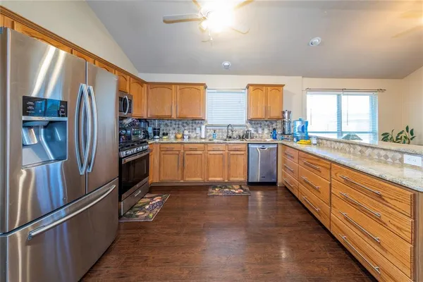 a large kitchen with stainless steel appliances granite countertop a refrigerator a sink dishwasher a stove with wooden cabinets and floor