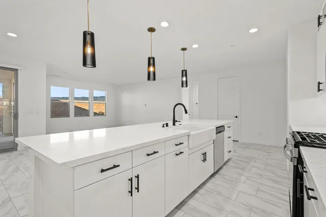 a large white kitchen with a stove a sink a refrigerator and white cabinets with wooden floor