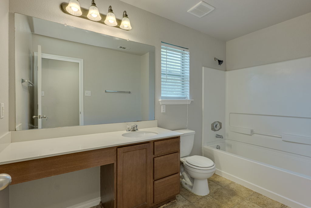 210 Cushman Drive Kyle, TX 78640 - Photo 19 of 21 Bathroom featuring a wood-finish vanity with a built-in sink, a full-width mirror, and a combination tub and shower with white surround