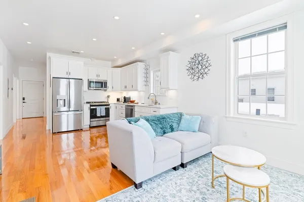 a living room with stainless steel appliances furniture a rug and a kitchen view