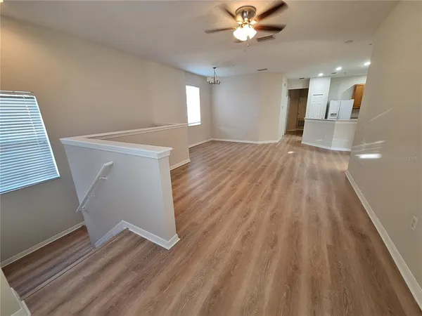 an empty room with wooden floor chandelier fan and windows