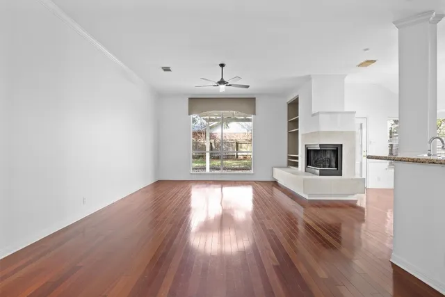 a view of an empty room with wooden floor and a kitchen