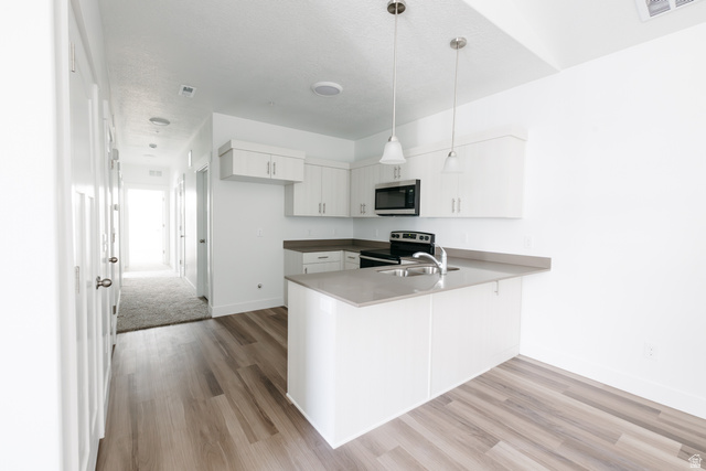 4653 South Alder Drive, Unit H304 Mapleton, UT 84664 - Photo 6 of 14 Kitchen featuring white cabinets, a peninsula, hanging light fixtures, stainless steel appliances, and light wood-type flooring