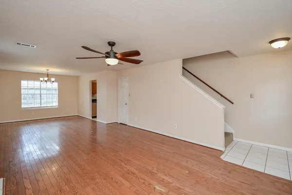 a view of an empty room with wooden floor and a ceiling fan