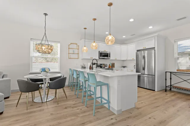 a kitchen with stainless steel appliances kitchen island granite countertop a stove a refrigerator a oven a sink with a dining table and chairs with wooden floor