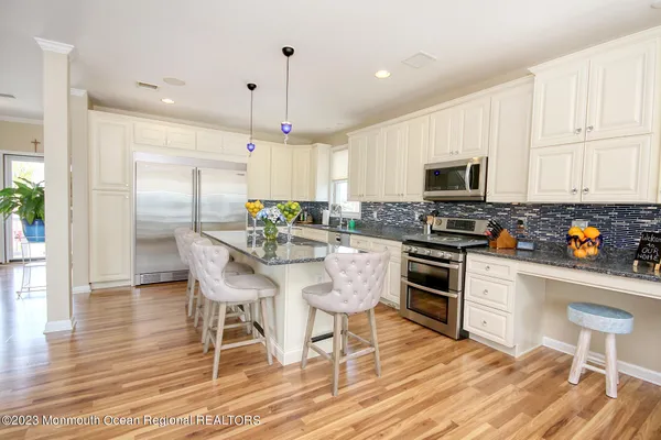 a kitchen with stainless steel appliances granite countertop a stove a sink a microwave a refrigerator white cabinets and a dining table with wooden floor
