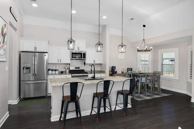 a kitchen with stainless steel appliances kitchen island granite countertop a dining table chairs and white cabinets