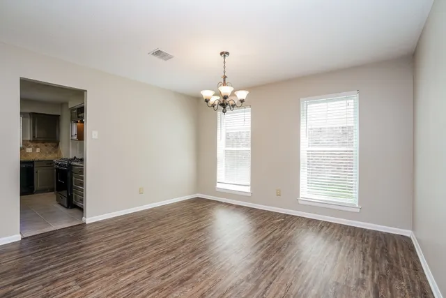 an empty room with wooden floor chandelier and windows