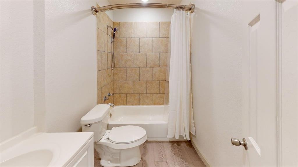 2554 Marfa Avenue Dallas, TX 75216 - Photo 19 of 19 Bathroom featuring shower / bathtub combination with curtain, vanity, light wood-style floors, and a textured wall