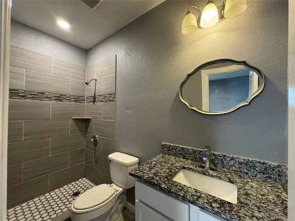 a bathroom with a granite countertop toilet sink mirror and shower