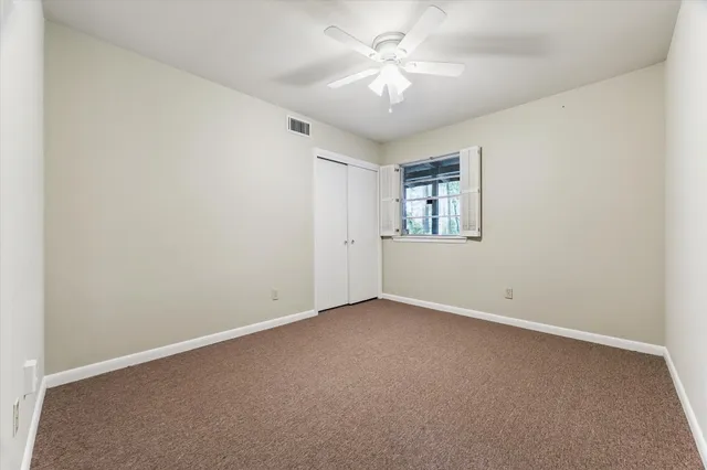 an empty room with chandelier fan and windows