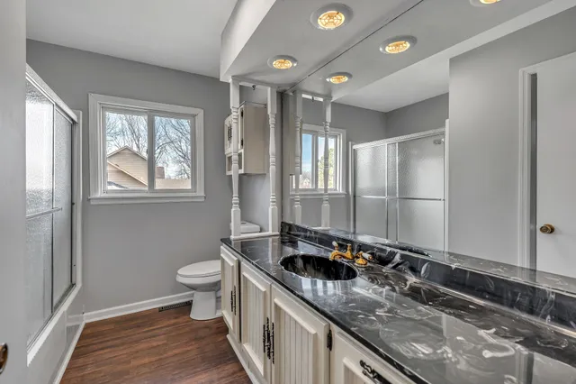 a bathroom with a granite countertop sink a toilet a mirror and window