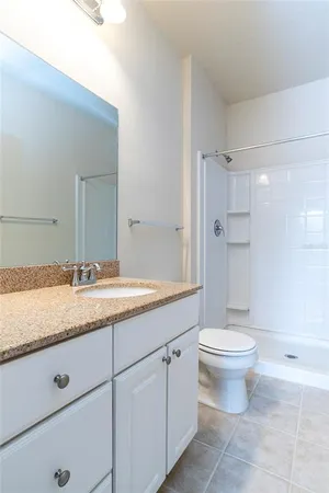 a bathroom with a granite countertop sink a toilet a mirror and shower