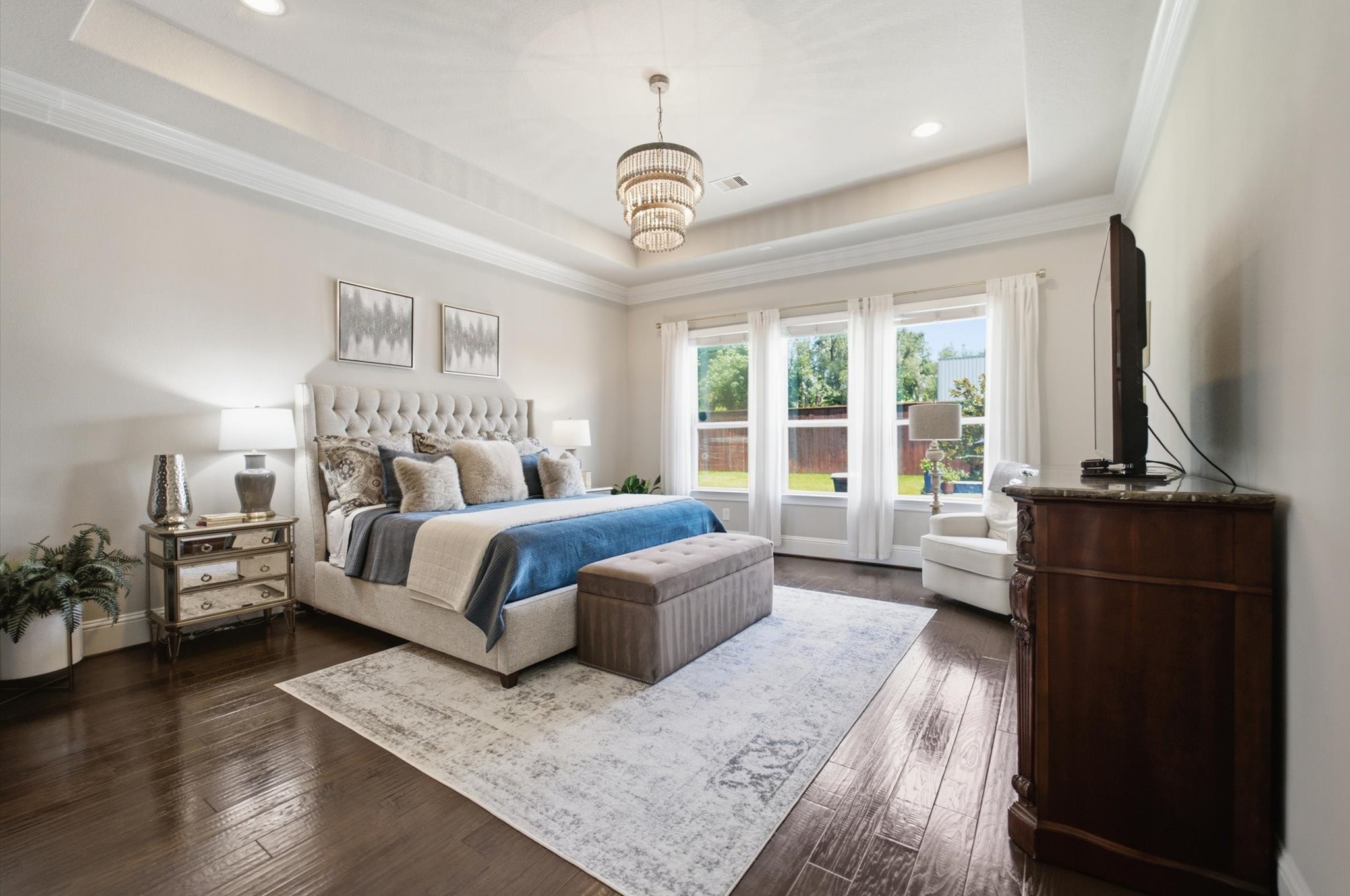 23722 Thortons Park Lane Spring, TX 77389 - Photo 10 of 48 This spacious bedroom features elegant hardwood floors, a plush bed with a tufted headboard, and abundant natural light from large windows. The room is tastefully decorated with neutral tones and includes a stylish chandelier, creating a cozy yet sophisticated ambiance.