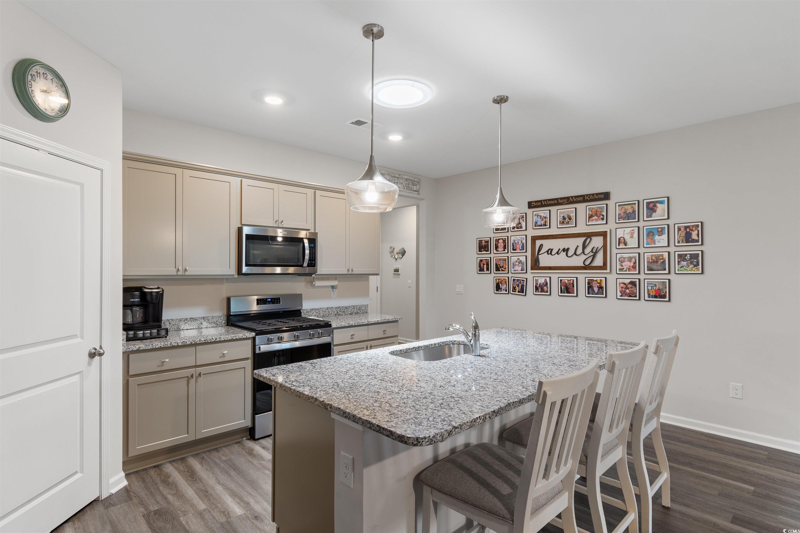 2438 Polaris Path Myrtle Beach, SC 29577 - Photo 7 of 40 Kitchen with appliances with stainless steel finishes, dark wood finished floors, a breakfast bar area, light stone counters, and pendant lighting