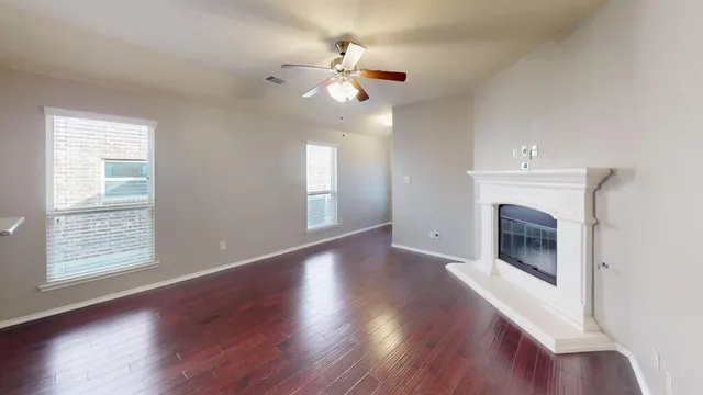 an empty room with wooden floor fireplace and windows