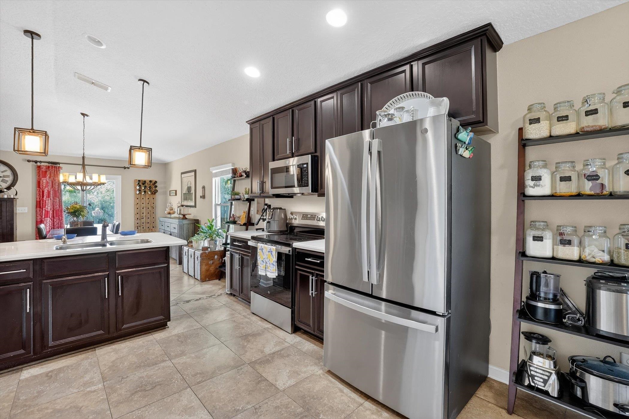 137 Fallen Timber Way St. Augustine, FL 32084 - Photo 21 of 45 Kitchen featuring dark wood finish cabinets, stainless steel appliances, light countertops, a chandelier, and light tile patterned floors