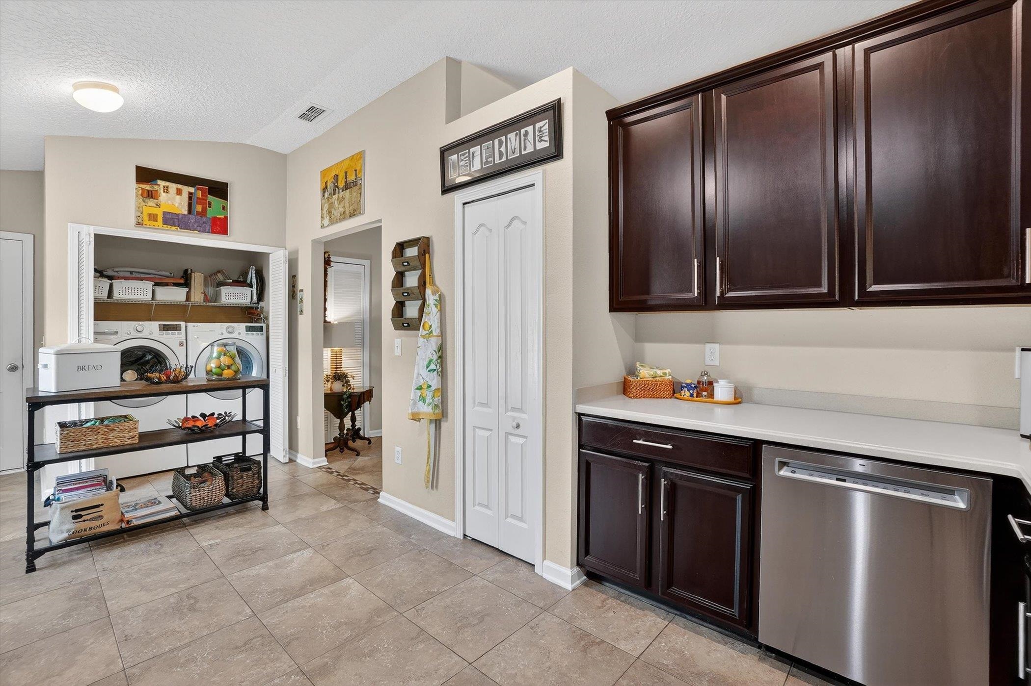 137 Fallen Timber Way St. Augustine, FL 32084 - Photo 44 of 45 Kitchen with stainless steel dishwasher, dark wood finish cabinetry, separate washer and dryer, and light tile patterned floors