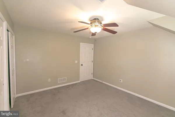 an empty room with a chandelier fan and closet area