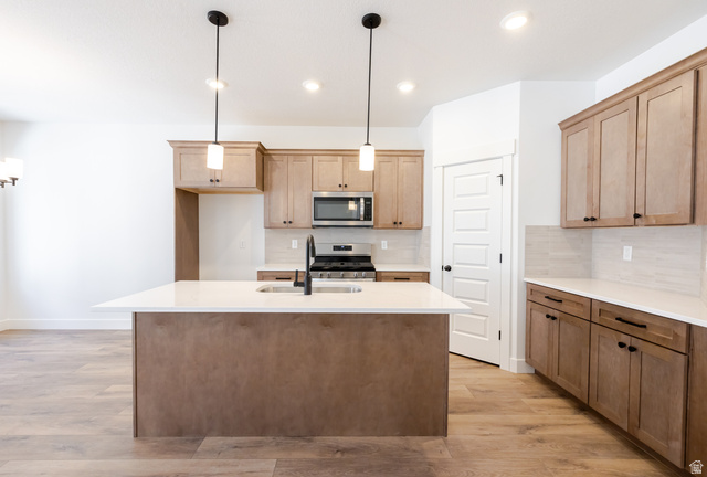 4809 Olive Avenue, Unit 417 Mapleton, UT 84664 - Photo 4 of 18 Kitchen with light wood-style floors, light stone countertops, a kitchen island with sink, stainless steel appliances, and hanging light fixtures