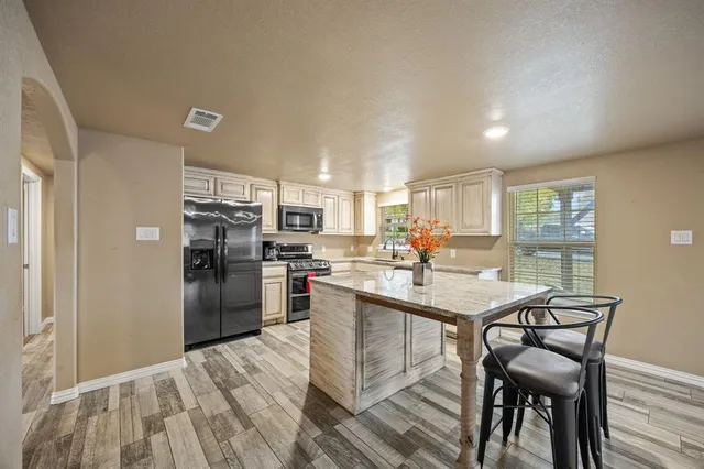 a kitchen with stainless steel appliances a refrigerator a stove a dining table and chairs with wooden floor