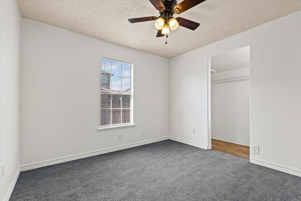 205 Cisneros Street Kyle, TX 78640 - Photo 7 of 17 Unfurnished bedroom with carpet, a textured ceiling, a ceiling fan, and a spacious closet