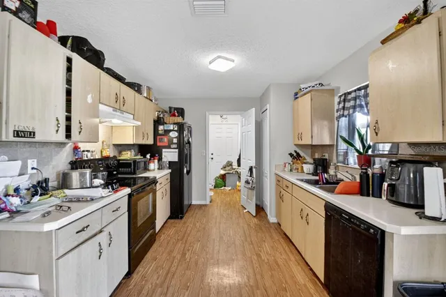 a kitchen with stainless steel appliances a stove top oven a sink a refrigerator white cabinets and wooden floor